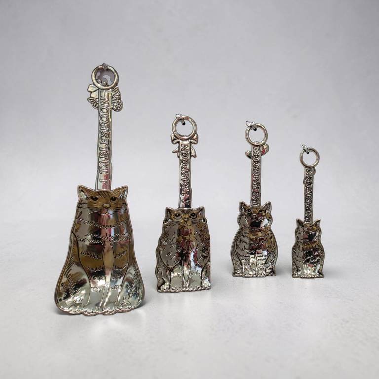 Four polished silver tone cat-shaped zinc alloy measuring spoons on a metal ring, fanned out and displayed against a plain white background
