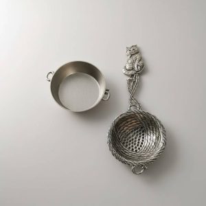 Polished silver tone cat-shaped loose leaf tea strainer with woven basket design, shown with matching stainless steel drip bowl
